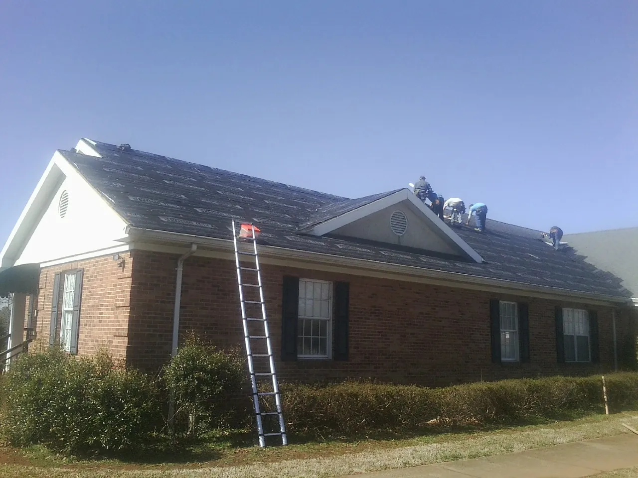 Crew tearing shingles off a brick ranch roof with a ladder set — Emergency Roof Repair work by our crew in Wakarusa