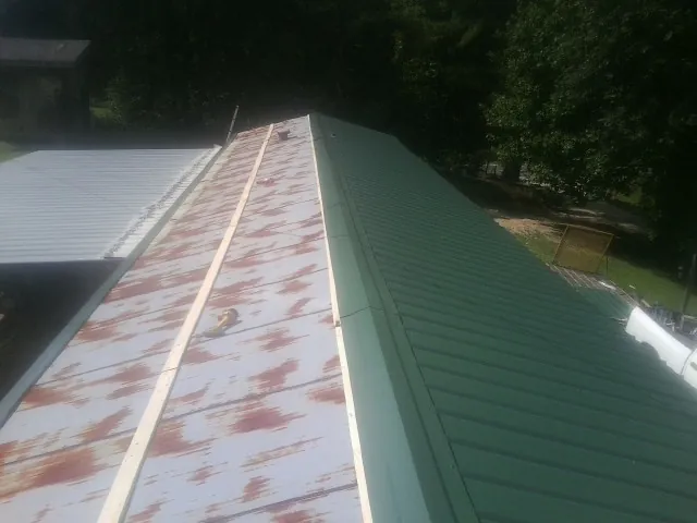 Old rusted panels beside newly installed green metal roofing — Wind Damage Roof Repair by Roofing Brothers in Wakarusa