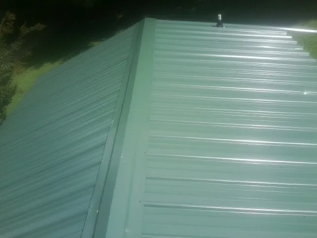 New green metal panels meeting at the ridge of a roof — Flat Roof Repair work by our crew in Wakarusa
