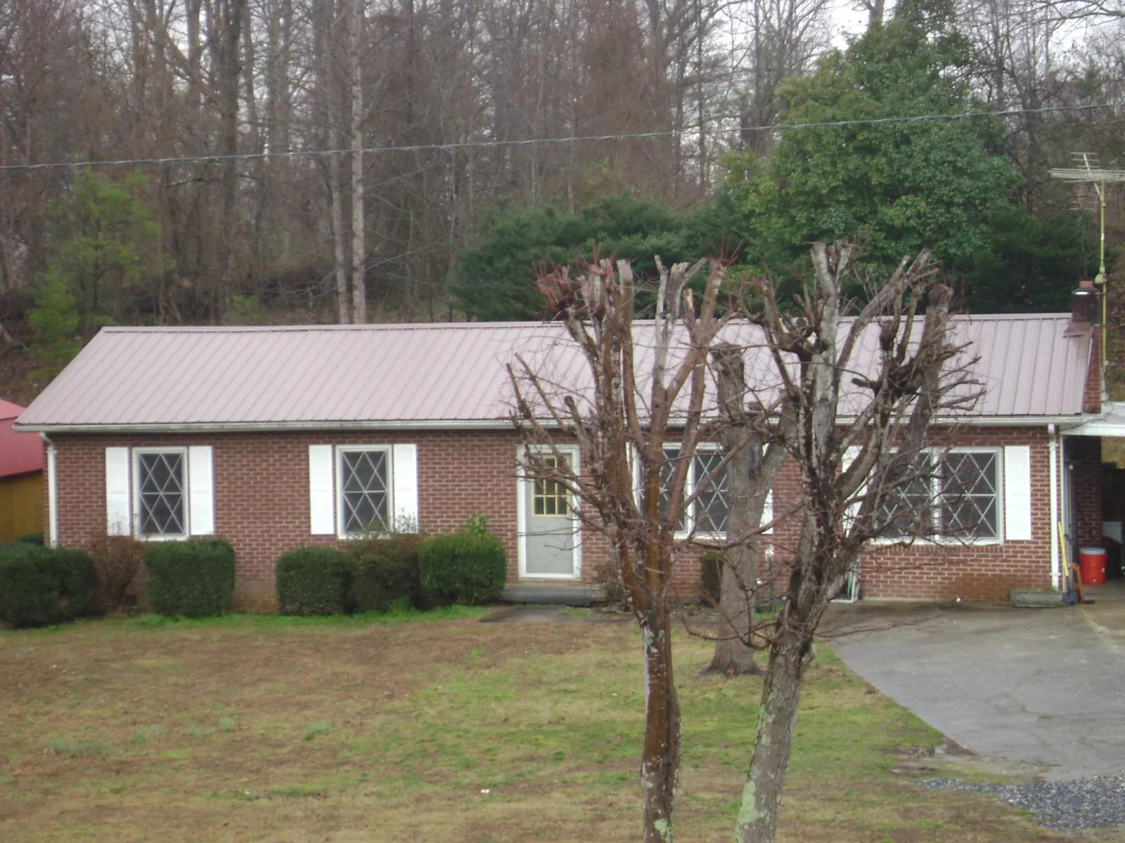 Mauve metal roof on a brick ranch home behind bare trees in Wakarusa