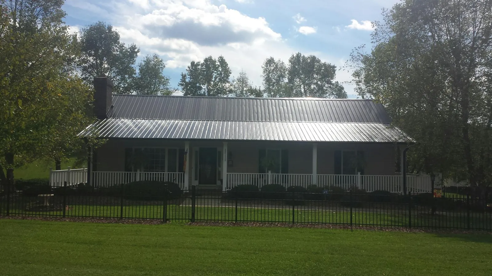 Gray metal roof on a brick ranch with a full width front porch — Gutter Guard Installation work by our crew in Wakarusa